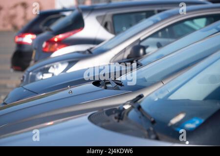 Many cars parked next to each other in a row in a parking lot. Focus on the wipers, nozzles and windshield of the second car Stock Photo