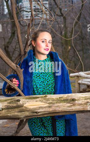 Dressing in blue faux fur coat and patterned dress, a pretty woman is looking at you in a chilling winter Stock Photo