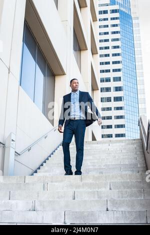 A young handsome black businessman is walking down on steps from a business building. Stock Photo