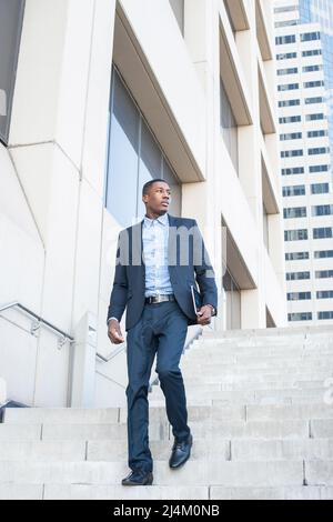 A young handsome black businessman is walking down on steps from a business building. Stock Photo