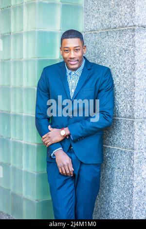 A young handsome black guy is standing in the corner between two walls, smiling. Stock Photo