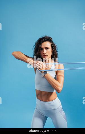 Young fit woman doing workout using stretch band on blue bacground Stock Photo