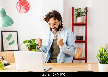 Excited young man reading online good news on laptop computer at home Stock Photo