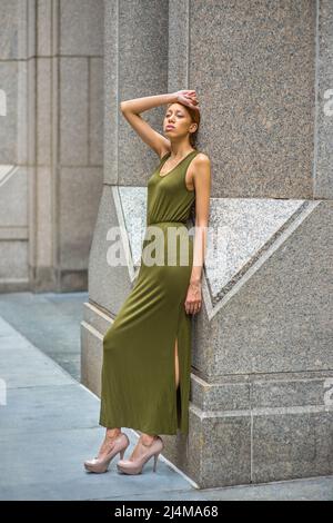 Woman Relaxing Outside. Dressing in a green Maxi Tank Dress, high heels, a hand resting on forehead,   a young black lady is leaning back on columns o Stock Photo