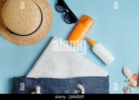beach bag with beach accessories on a colored background top view. Sunscreen, towel, glasses, hat. Stock Photo