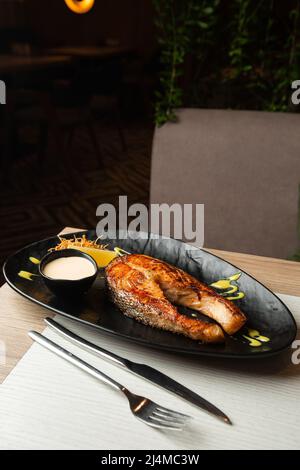 One piece of baked salmon steak grilled lemon and salt on a dark plate with white sauce Stock Photo