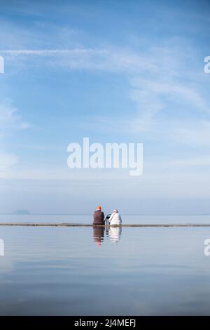 An elderly couple sit on the beach at Weston-super-Mare, Somerset Stock Photo