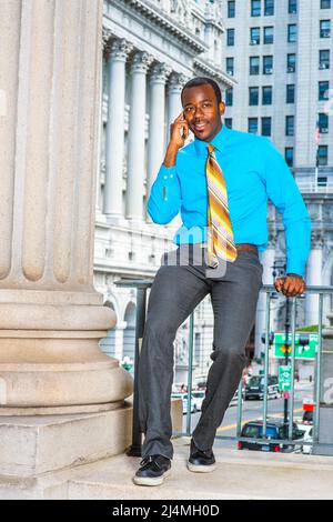 Dressing in a blue shirt, gray pants and black leather shoes, one hand  touching his chin,