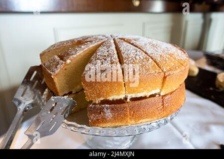 A Victoria sponge cake filled with butter icing and jam has been cut into slices ready for serving. Stock Photo