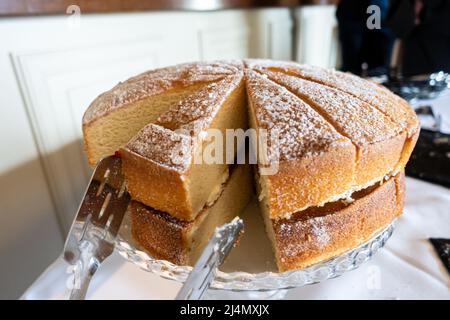 A Victoria sponge cake filled with butter icing and jam has been cut into slices ready for serving. Stock Photo