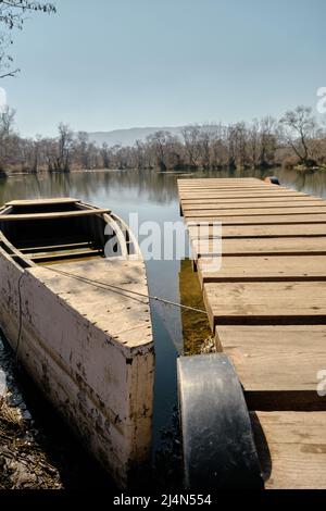 Small fishing boat and small pier made of wood with dried trees and reflection on water pond background in Bursa. Stock Photo