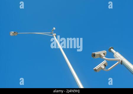 Looking up at surveillance closed circuit television cameras and streetlight isolated against a blue sky Stock Photo