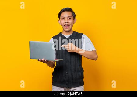 Excited handsome young man pointing at laptop on yellow background Stock Photo