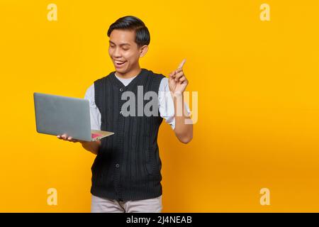 Excited young handsome businessman having a creative idea while holding a laptop on yellow background Stock Photo