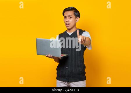 Angry young handsome man having a creative idea while holding a laptop on yellow background Stock Photo