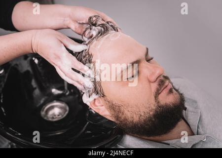 Hairstylist washing client's hair in barber shop. A young bearded man of Caucasian appearance at a reception at a barber shop. The process of cutting Stock Photo