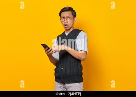 Surprised handsome young man using and texting smartphone on yellow background Stock Photo