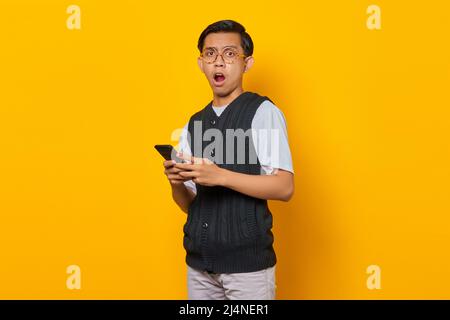 Portrait of a surprised handsome young man using smartphone on yellow background Stock Photo