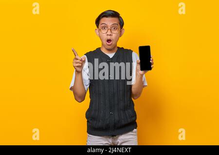 Shocked Asian man showing blank smartphone screen and finger pointing at empty space Stock Photo