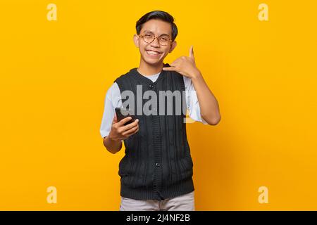 Portrait of cheerful Asian young man holding smartphone and doing phone gesture with hands Stock Photo