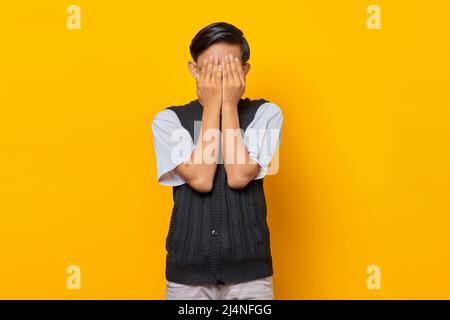 Portrait of handsome young man covering face with palms over yellow background Stock Photo