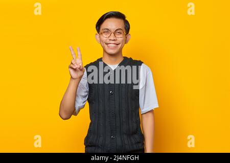 Portrait of cheerful Asian man showing peace sign over yellow background Stock Photo