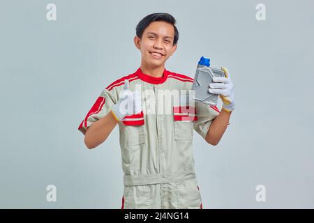 Portrait of cheerful handsome man wearing mechanic uniform holding plastic bottle of engine oil and showing approval with thumb up Stock Photo