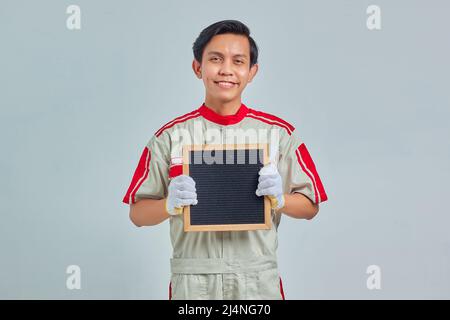 Portrait of cheerful young mechanic wearing uniform showing blank board on gray background Stock Photo