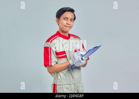 Cheerful young male mechanic taking notes on clipboard on gray background Stock Photo