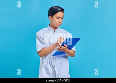 Smiling young male nurse taking notes on clipboard on blue background Stock Photo