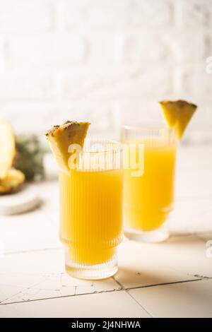 Pineapple cocktail or juice in two glasses with ice on white background with palm leaves Stock Photo