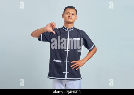 Portrait of angry asian young man wearing karate and pointing at himself with finger over gray background Stock Photo