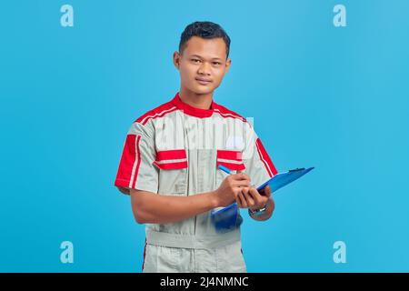 Image of smiling asian handsome man wearing mechanic uniform taking notes on clipboard Stock Photo