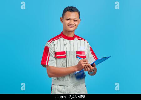 Image of cheerful asian handsome man wearing mechanic uniform taking notes on clipboard Stock Photo