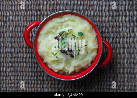 Mashed potatoes with radish microgreens in a red saucepan close up, top view Stock Photo