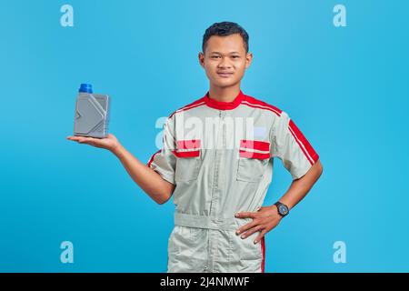 Portrait of smilling young asian mechanic  showing engine oil plastic bottle in palm over blue background Stock Photo