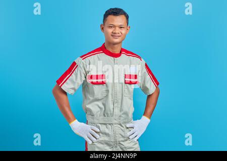 Portrait of smiling young Asian mechanic holding hands confidently over blue background Stock Photo