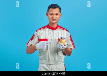 Portrait of smiling young Asian mechanic carrying cup of coffee in hand over blue background Stock Photo