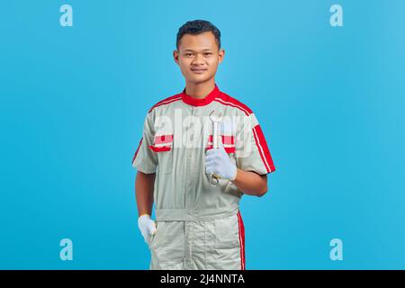 Portrait of smiling young Asian mechanic holding wrench in hand and looking at camera over blue background Stock Photo
