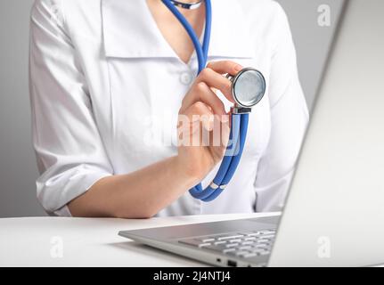 Doctor with stethoscope speaking to patient through video chat. Woman in lab coat advising client with illness, injury, using laptop. Online medicine consultation and diagnostics concept. photo Stock Photo