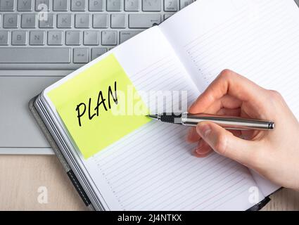 Woman hand closeup writing plans in notebook. Time management, organizing concept. Female sitting at table with laptop and taking notes. High quality photo Stock Photo