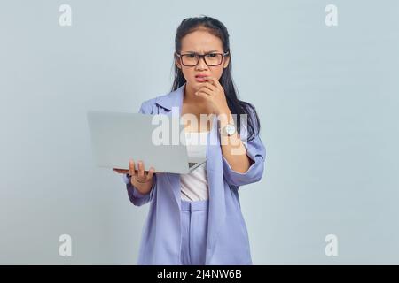 Portrait of scared young Asian woman standing using laptop and biting nails isolated on white background Stock Photo