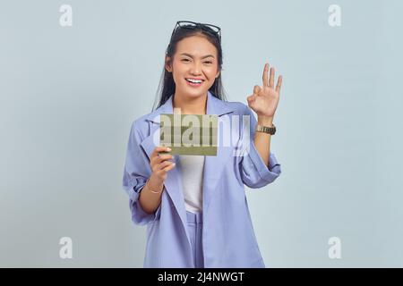 Portrait of smiling young Asian woman holding vehicle book and showing thumbs up gesture, Approving expression looking at camera showing success isola Stock Photo