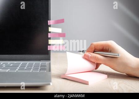 Woman hand taking memo notes at sticky papers. Female sitting at table with laptop and recording with pen key words and phrases, plans, thoughts. High quality photo Stock Photo