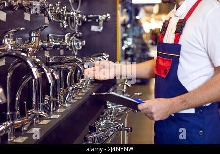 Male worker checks assortment on showcase with stainless steel water taps in plumbing store. Stock Photo
