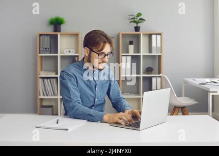 Happy student or office worker sitting at desk and working on his laptop computer Stock Photo