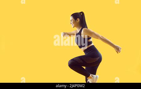 Beautiful smiling female athlete running and jumping isolated on vivid yellow background. Stock Photo
