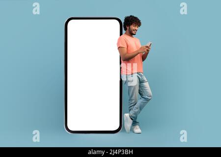 Cool indian guy leaning on huge smartphone, using cell phone Stock Photo