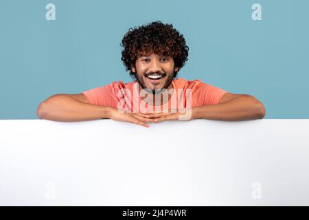 Relaxed bearded indian guy leaning on empty board for advertisement Stock Photo