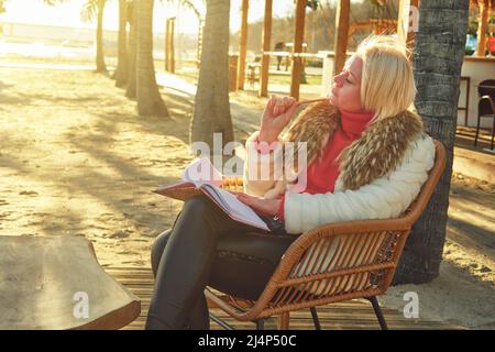A middle-aged woman with blonde hair sits in a street cafe.  Stock Photo